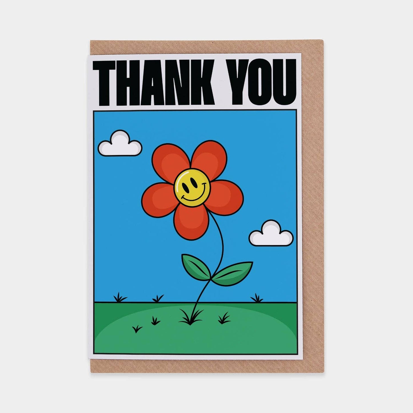 Greeting card with a red flower with a smiley face, blue sky, and green grass on a white background.