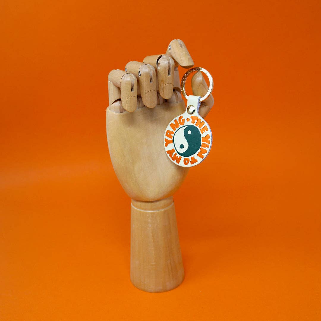 Wooden hand holding a keychain with a yin-yang symbol on an orange background