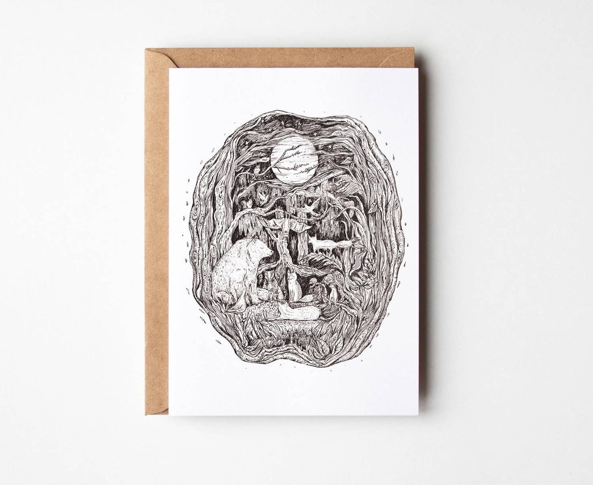 A white greeting card by Helen Drake with a detailed black ink illustration of a surreal forest scene featuring a cat, a tree, and a basketball, shown with a brown kraft envelope on a light gray background.