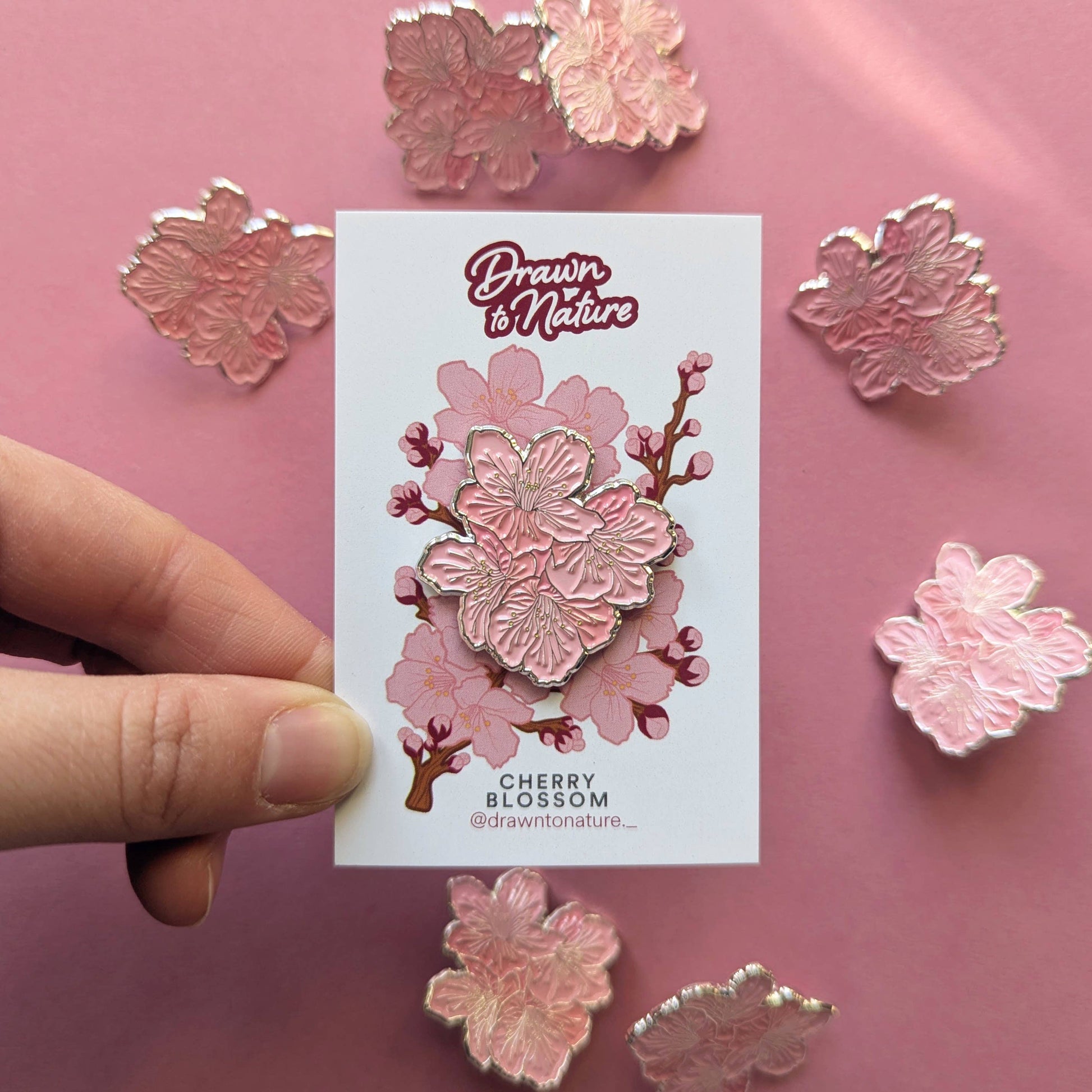 Cherry blossom pin on a card held by a hand with pink floral pins in the background.