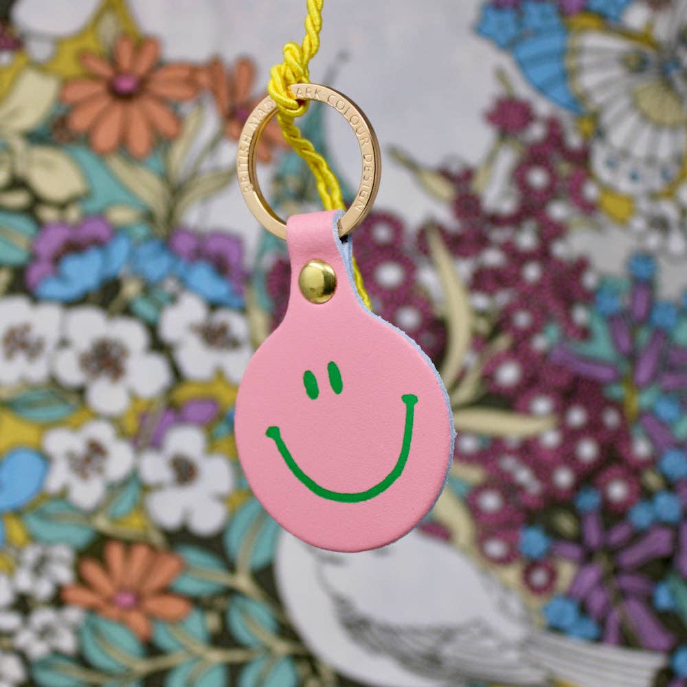 Pink smiley face keychain with a gold ring on a colorful floral background