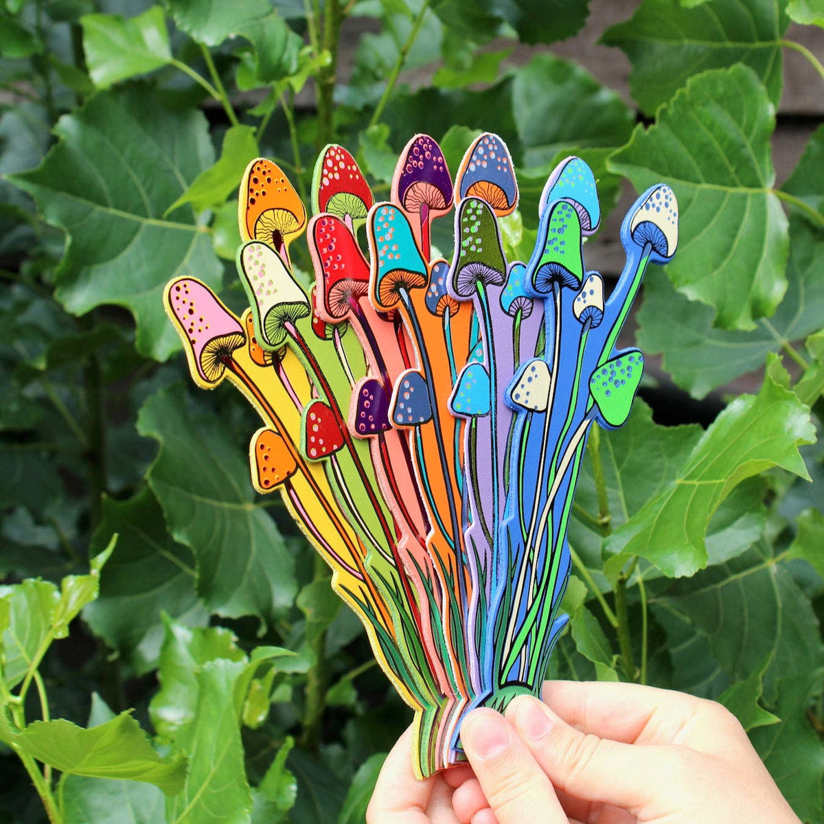 Colorful mushroom-shaped objects held in front of green leaves