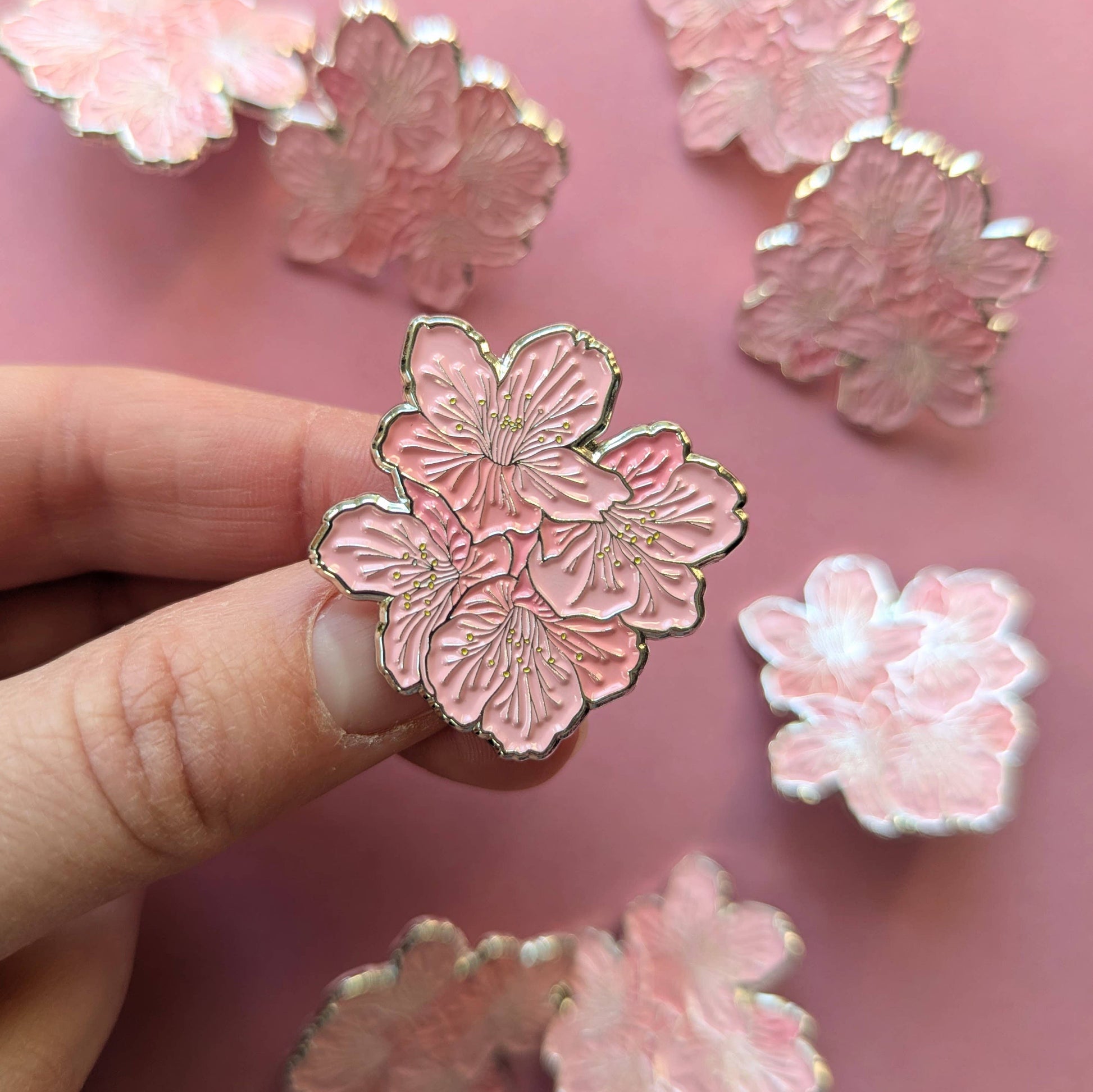 Pink floral pin held by a hand with more pins on a pink background
