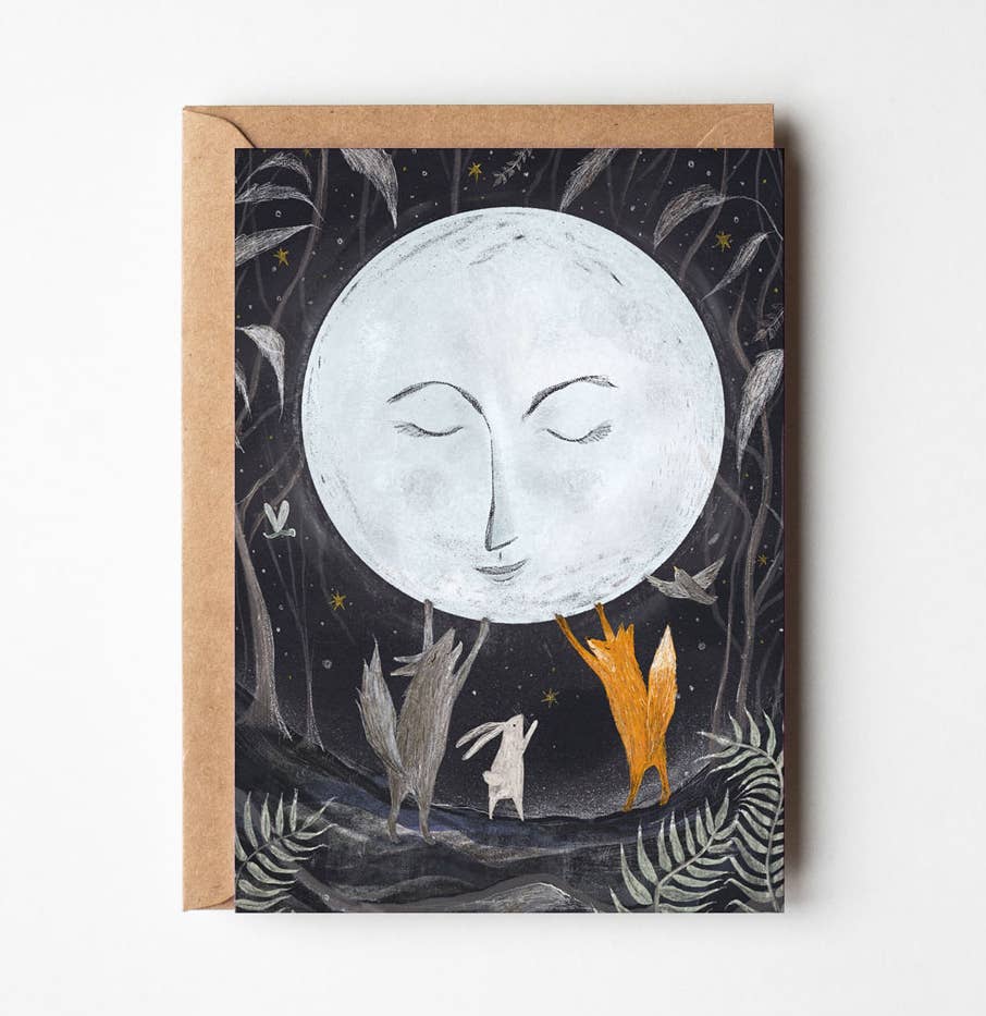 A square greeting card with a kraft envelope, featuring whimsical fantasy artwork of a large sleeping moon over small animals including a fox, rabbit, and bird against a dark starry background.