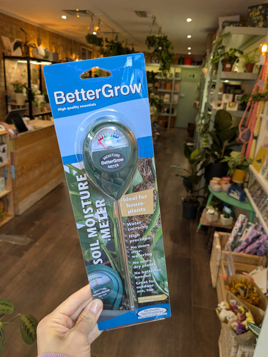 BetterGrow soil moisture meter packaging held in a store with plants and shelves in the background